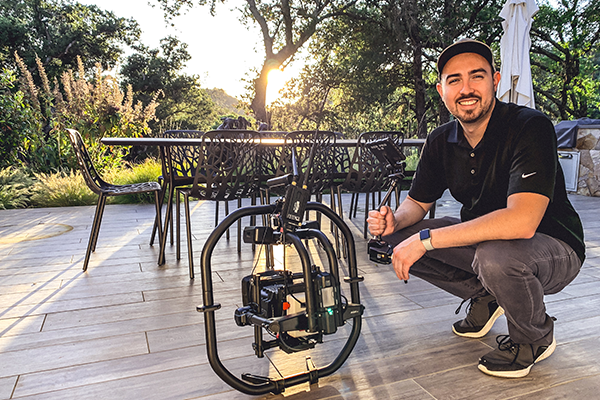 Promise Wine Still 1 Pour's Executive Producer Dominic crouched on a wooden deck next to a professional camera rig mounted on a stabilizer.