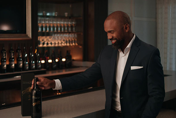 Charles Woodson dressed in a suit holding a bottle of Intercept Wines.