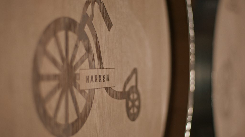 Harken Wines Case Study Photo 10 Close-up of a wooden barrel with a logo of a penny-farthing bicycle etched onto its surface, labeled HARKEN.