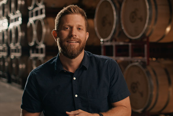 Harken Wines 600 A man standing in a warehouse with rows of large wooden barrels.