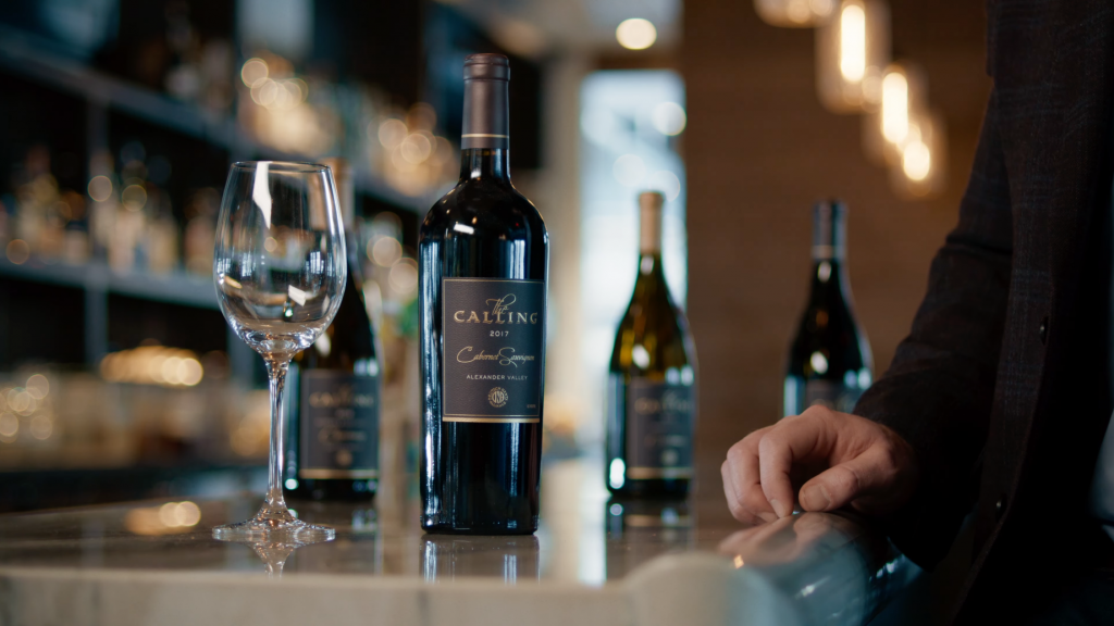 A wine bottle with the label 'The Calling' next to an empty wine glass.