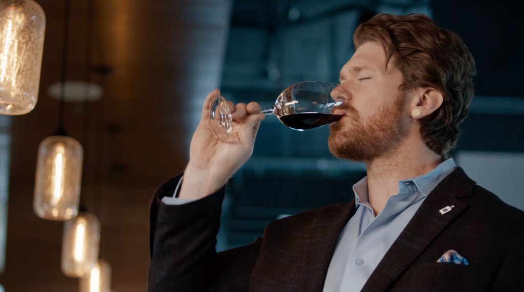 A person drinking red wine from a wine glass.