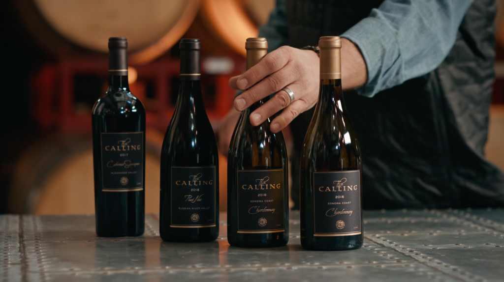 Four bottles of wine from 'The Calling' brand. A hand is holding the third bottle from the left.